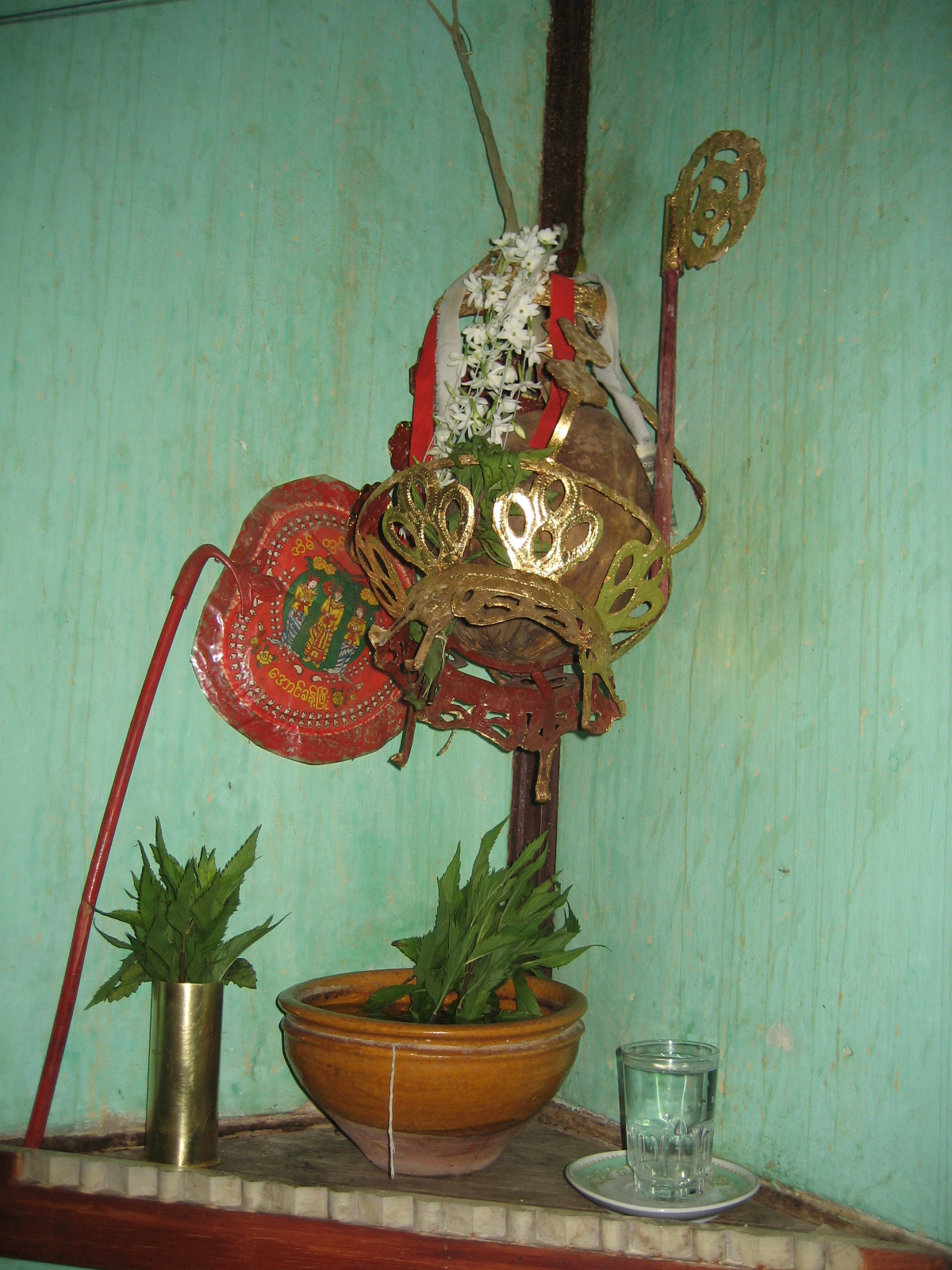 Nat figure (Burmese spirit-deity) — Nat oun coconut with its stalk intact hung in the southeast corner of a private home in Mandalay, in a gilded hanging ba
