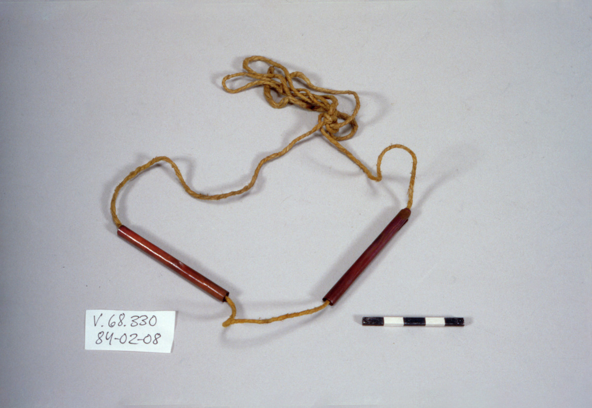 Takrut (inscribed scroll-tube) — A pair of red-lacquered takrut tubes on their waist cord, bought in Bangkok in 1887 — the museum called it simply "amulet"; the reading as takrut is this project's, from the form