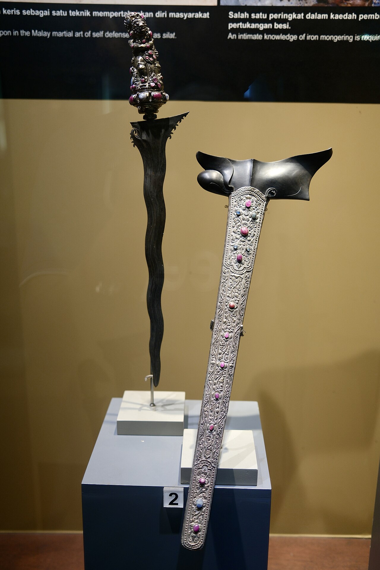 Keris / kris (the heirloom dagger) — The hilt has a copper ring at its base and is shaped like a squatting Hindu deity. The crosspiece is made of ivory and h