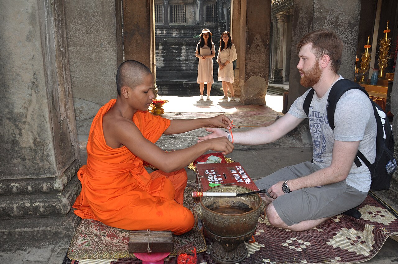 Sai sin (blessed cotton thread) — Buddhist monk gives blessed string bracelet (Sai Sin) to a tourist at Angkor Wat, Siem Reap Province, Cambodia.