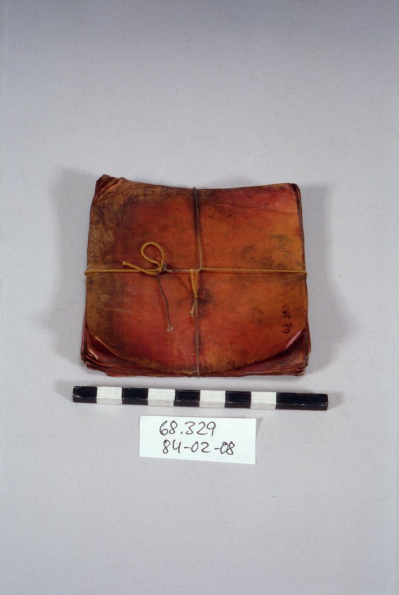 Pha yan (yantra cloth) — A tied stack of square red-lacquered sheets catalogued in 1887 as "sheet, amulet" — read here as yantra sheets (ผ้ายันต์ / ประเจียด); the museum does not say, so this is an inference