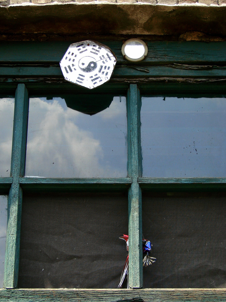 Bagua mirror — Taijitu within a frame of trigrams and a demon warding mirror, these charms photographed above a window in in a resident