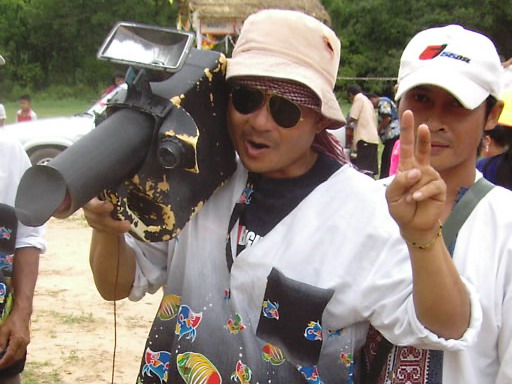 Palad khik (phallic waist charm) — Cameraman (with fake camera) at village Rocket Festival salutes author, Pawyi Lee
