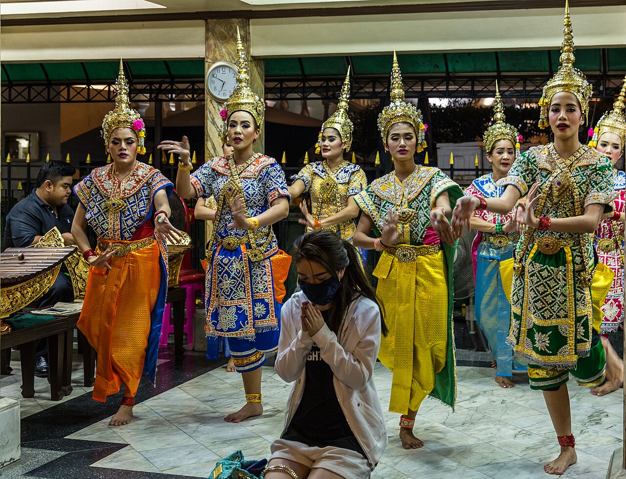 Four-faced Brahma pendant — A worshipper prays to the statue of Brahma at the Erawan Shrine (not shown), as a troupe of dancers perform a dance as a